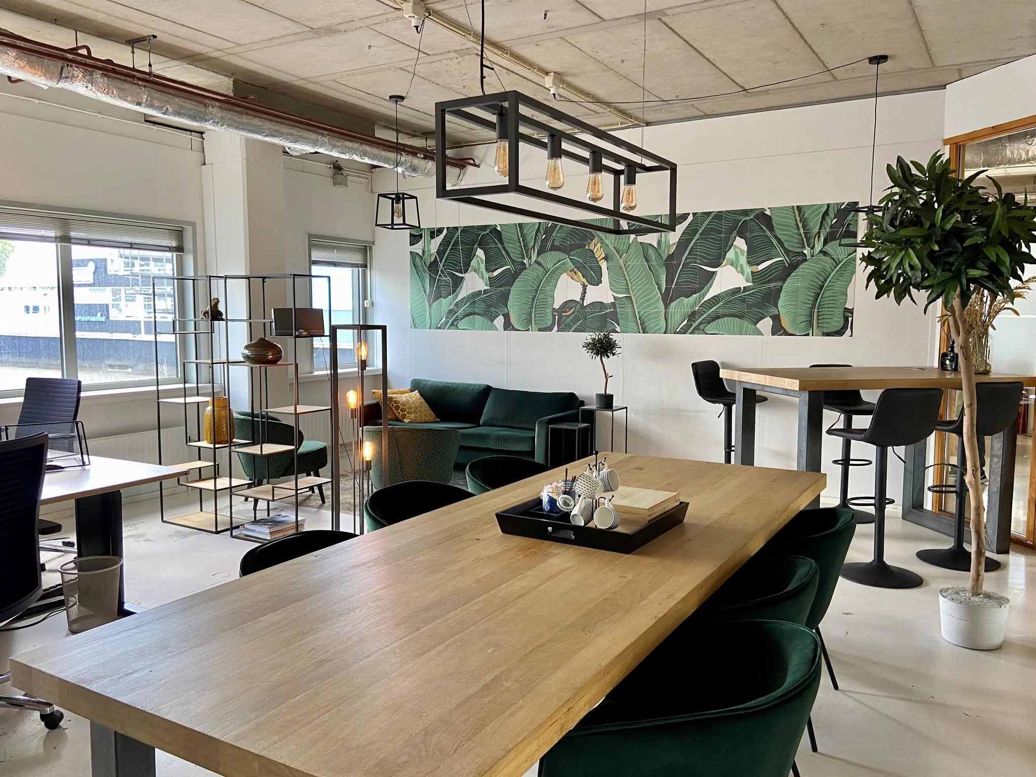 Moderne kantoorruimte aan de Anthony Fokkerweg met houten tafels, groene meubels en een tropisch wandpaneel.